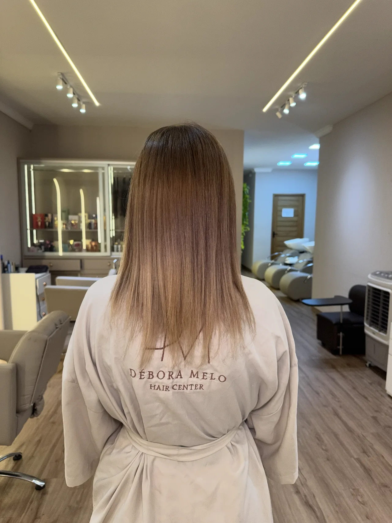 Cliente de roupão do salão, cabelo castanho na altura dos ombros, antes da aplicação.