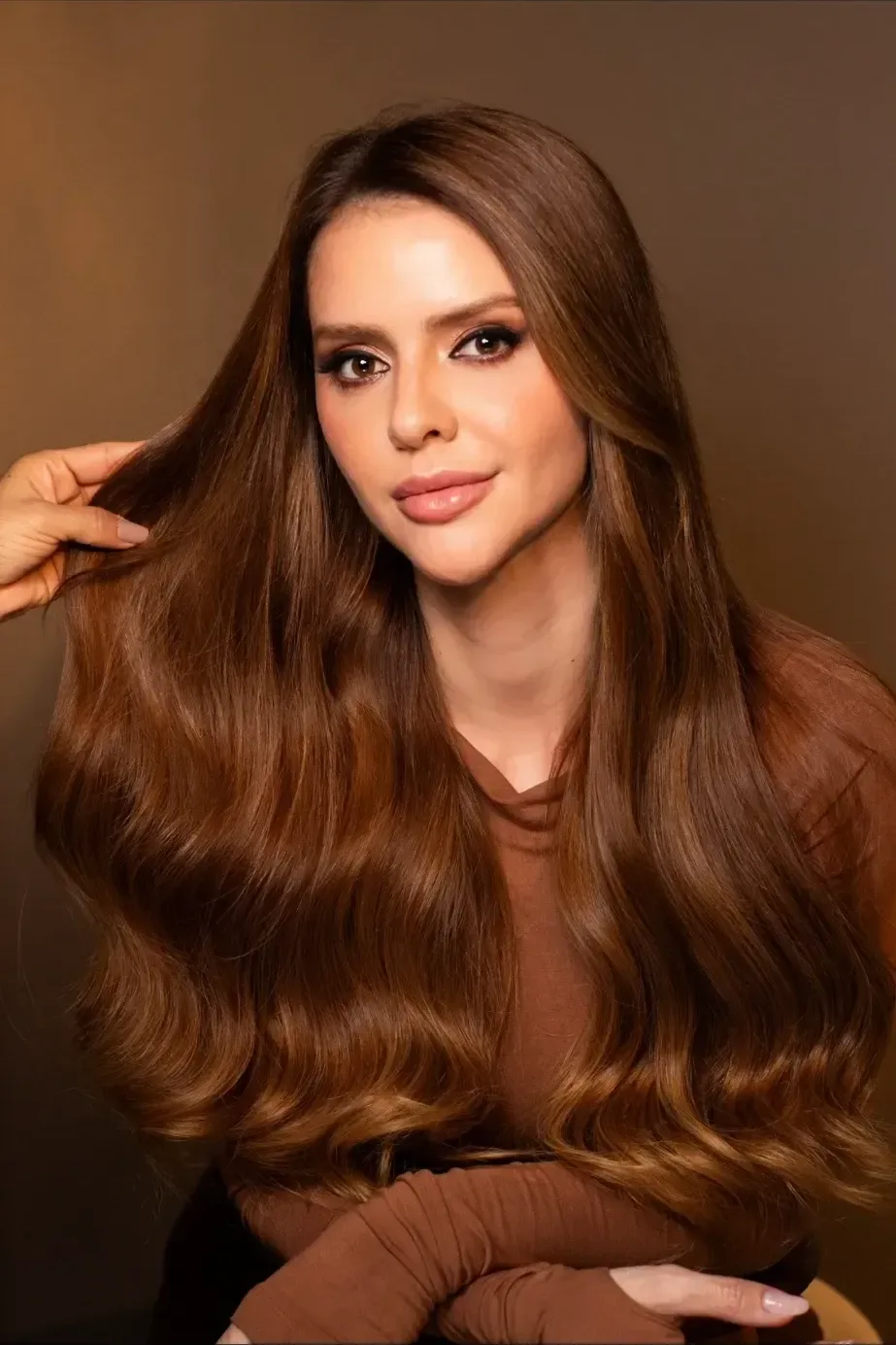 Modelo segurando o próprio cabelo castanho longo.